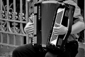A black and white photo of a street musician playing an accordion, showcasing the instrument and musician's hands.