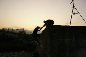 Two men in silhouette, one helping the other climb a wall at sunrise in Tirebolu, Türkiye.