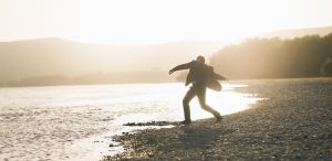 A man in a suit skips rocks by a serene lake at sunset, creating a tranquil and reflective scene.
