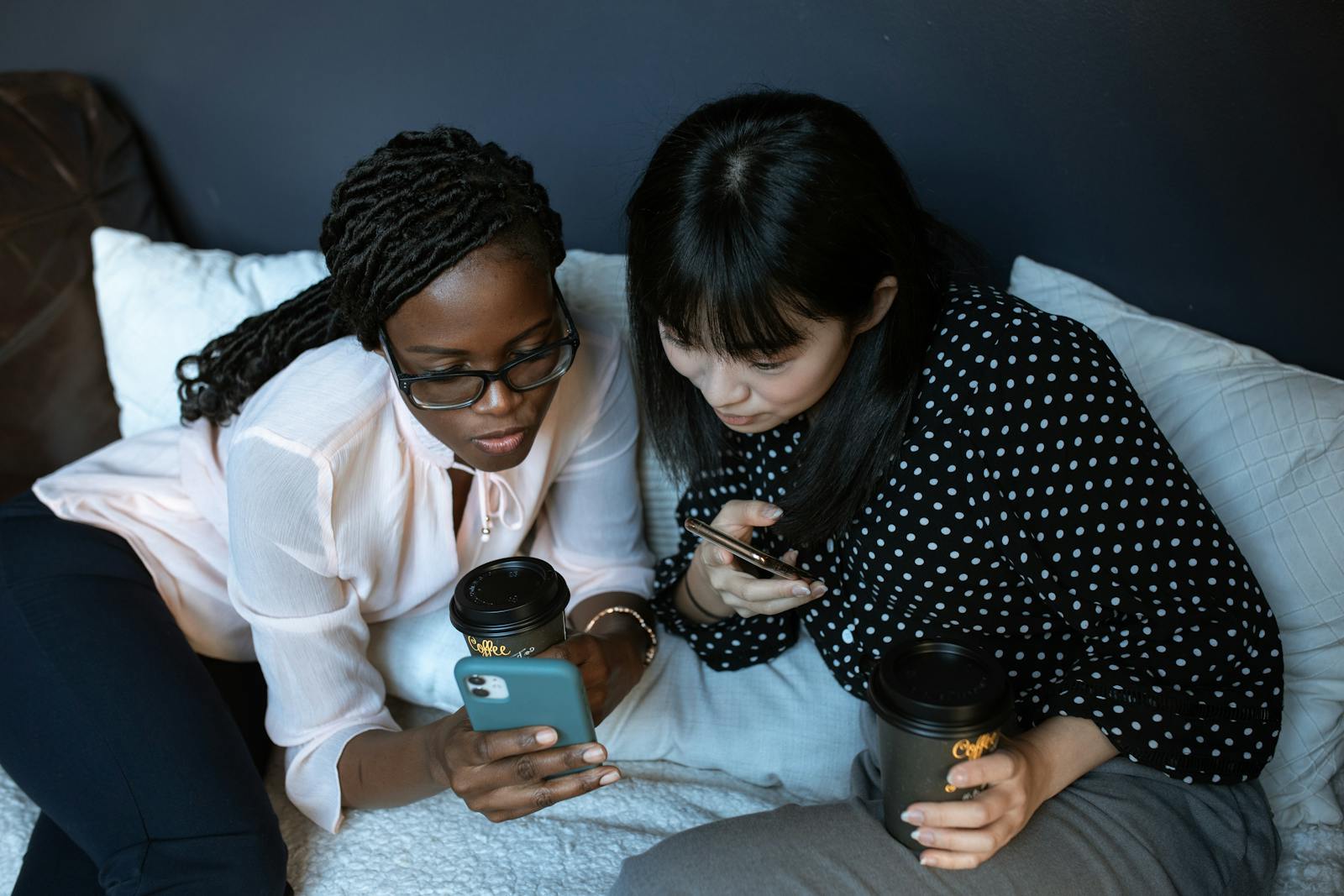 Two women engaged with their smartphones, sharing coffee and companionship indoors.