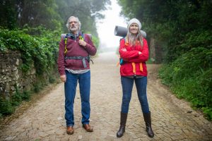 Senior couple hiking down a cobblestone path surrounded by lush greenery in Portugal.