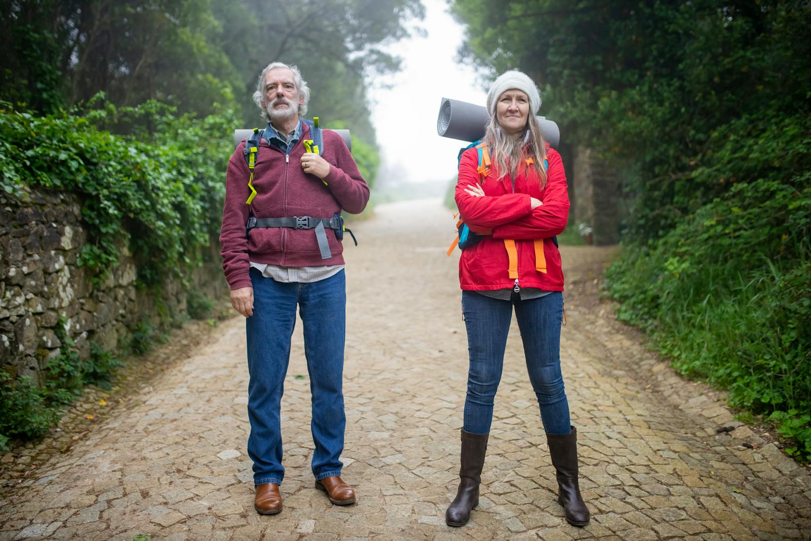 Senior couple hiking down a cobblestone path surrounded by lush greenery in Portugal.